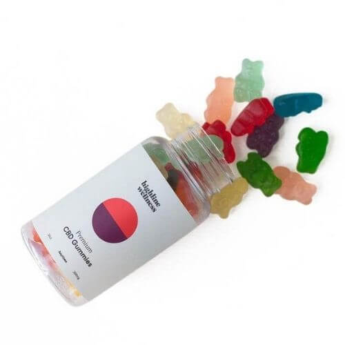 Clear bottle of Highline Wellness CBD gummy bears laying on its side with assorted gummy bears on white background.