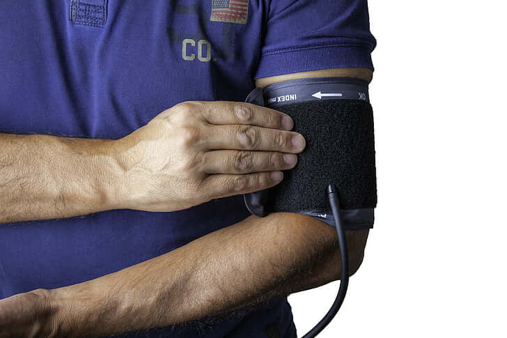 Man in blue T-shirt wearing blood pressure cuff on left bicep.