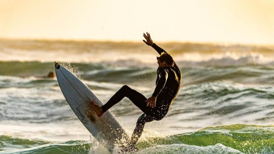 A surfer launching himself off of a wave and into the air with the sun setting in the background.