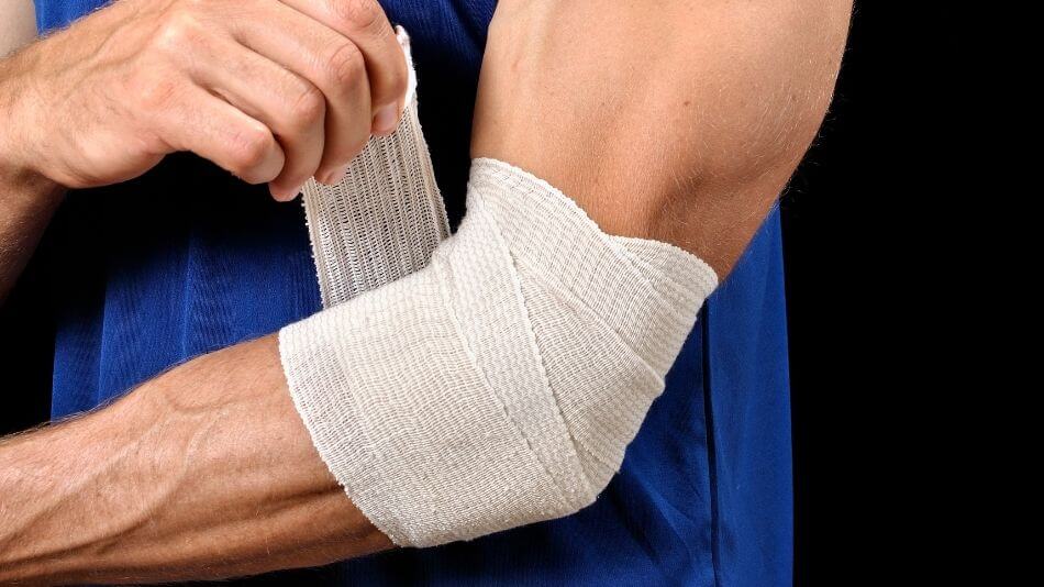 Man wearing a blue tank top wrapping an ace bandage on his elbow.