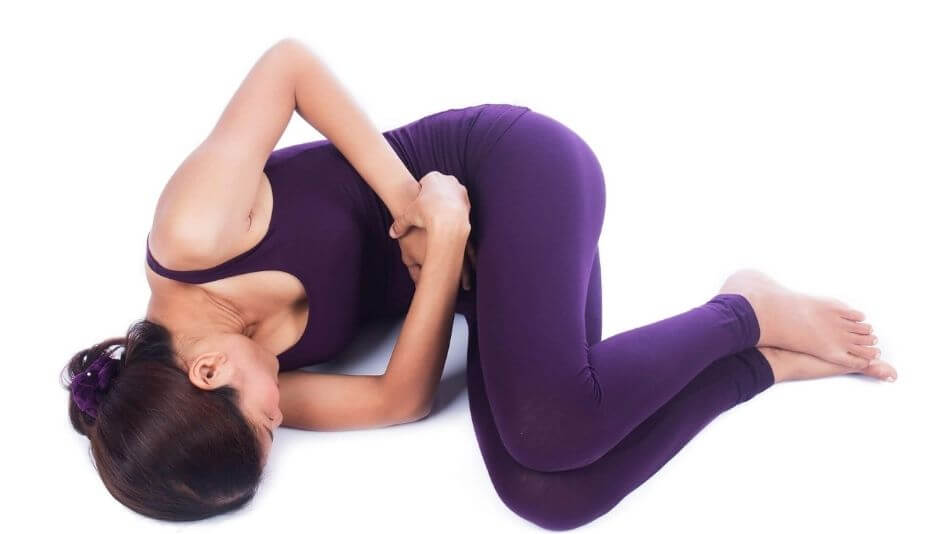 Brunette women wearing purple yoga cloths curled up on the floor holding her stomach in pain.