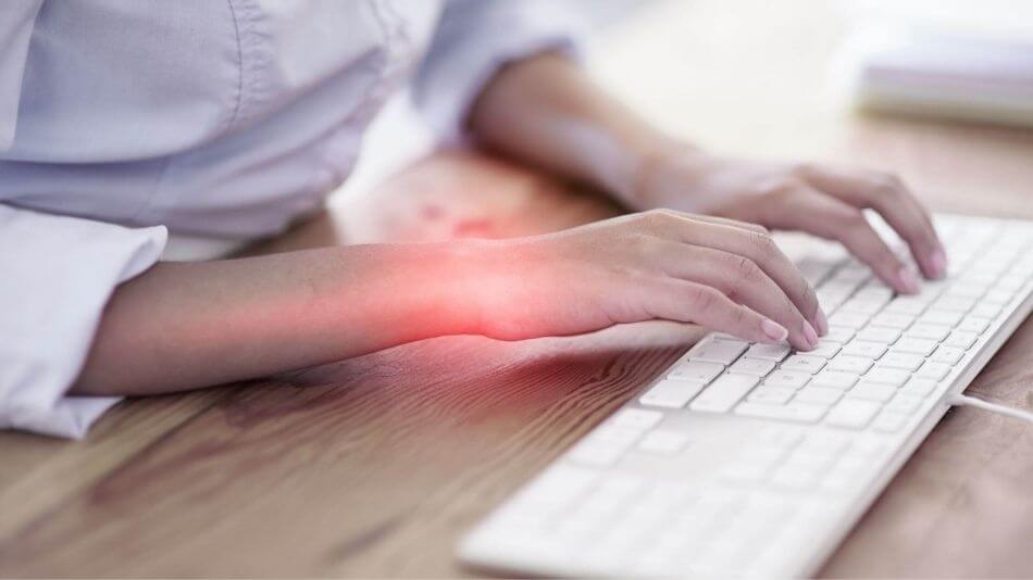 Women sitting at a desk typing on the keyboard with pain radiating from her left wrist.