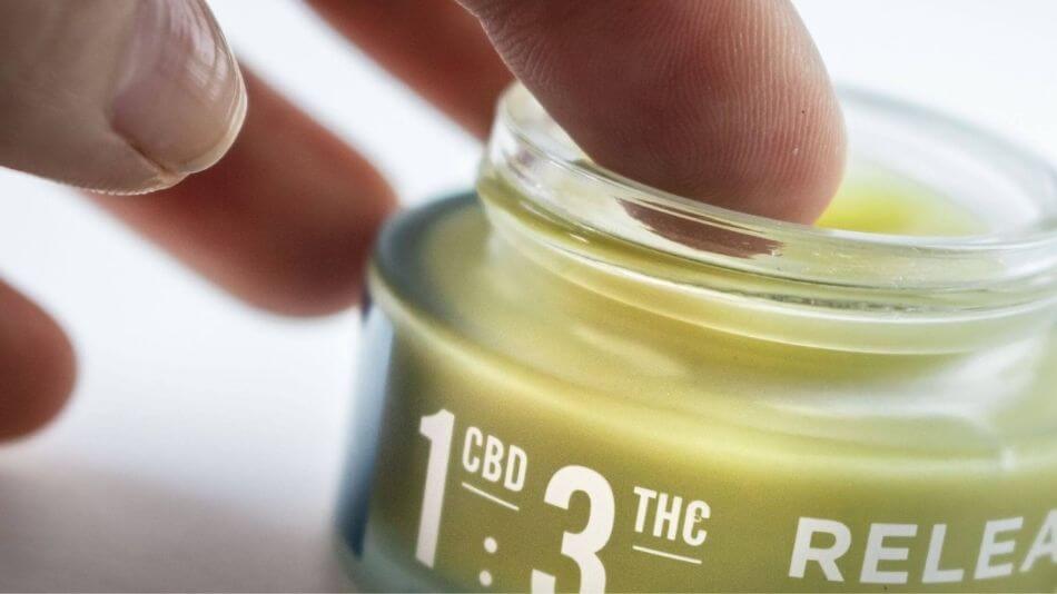 Mans hand reaching into a jar of 1:3 CBD to THC relief cream.