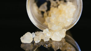 Glass jar laying on its side with CBD isolate crystals spilling out onto a black reflective surface.
