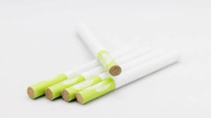 Four hemp cigarettes laying on a table with a fifth laying diagonal across them. The cigarettes are white with a lime green butt.