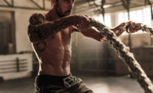 In shape guy with a tattoo sleeve on his right arm exercising with heavy ropes.