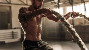 In shape guy with a tattoo sleeve on his right arm exercising with heavy ropes.