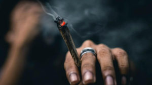 Lit joint being held in between a guys pointer finger and middle finger.