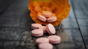 Topless orange prescription bottle on its side with pink circular pills coming out.