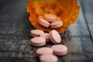 Topless orange prescription bottle on its side with pink circular pills coming out.
