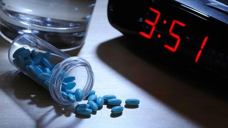 Clear bottle of blue oval shaped pills laying on its side with pills spilling out in front of a clock that reads 3:51.