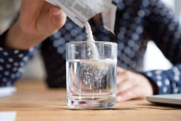 A man wearing a blue plad shirt pouring a packet of water soluble CBD into a glass of water.