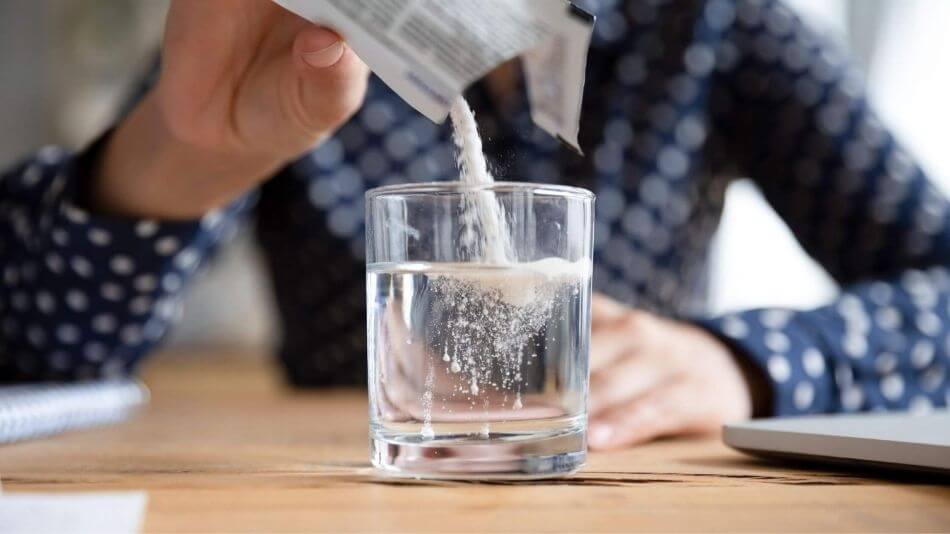 A man wearing a blue plad shirt pouring a packet of water soluble CBD into a glass of water.
