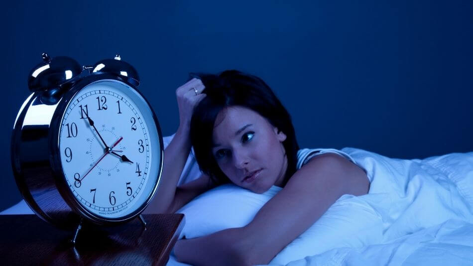 Dark haired women laying in bed staring at the clock because she can't sleep.