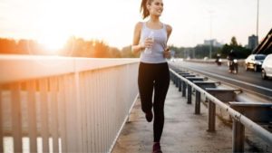 Brunette women in her late 20's running towards the camera with the sun setting behind her.