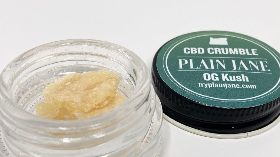 Plain Jane og kush CBD crumble in the jar with the lid behind and to the right.