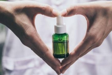 A green bottle of CBD being help by someone making a heart with their hands.