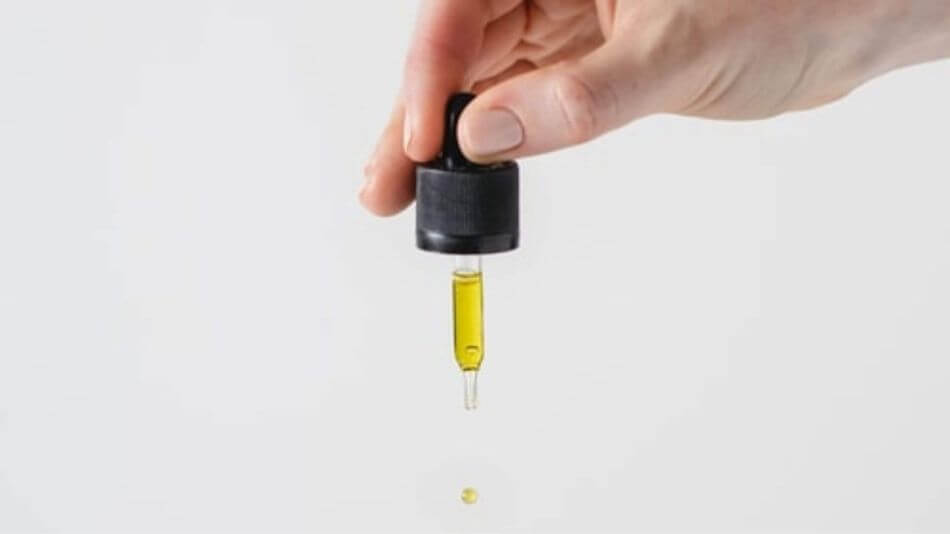 Womens hand holding an eyedropper full of CBD oil with one drop falling from the tip.