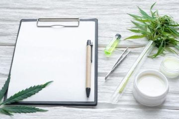 Clipboard with a blank sheet of paper and a pen sitting on top next to a test tube with cannabis.