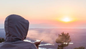 Man wearing a windbreaker hoodie smoking a joint during sunset.