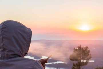Man wearing a windbreaker hoodie smoking a joint during sunset.