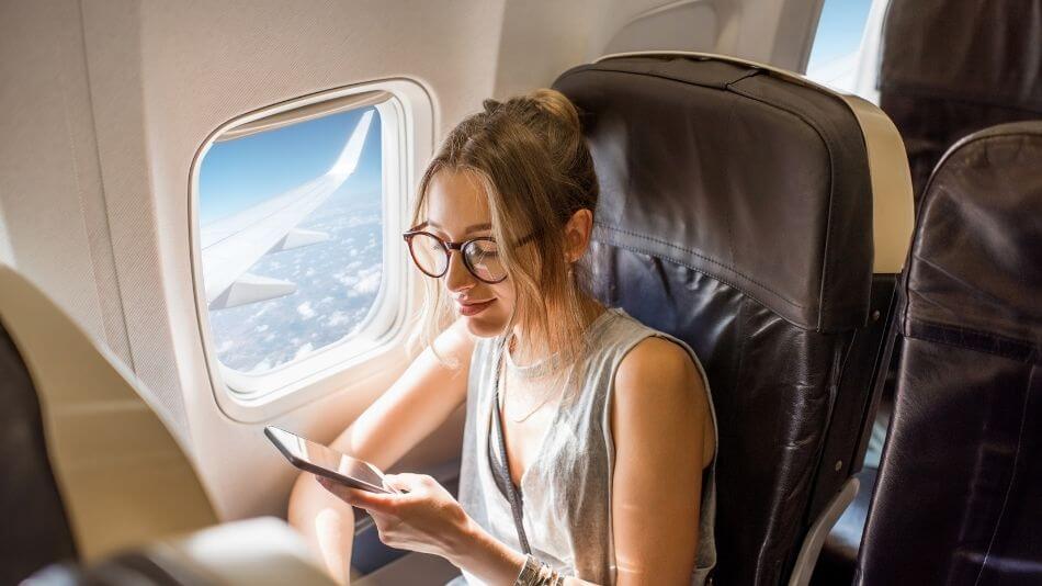 Dirty blond women in her twenties sitting on an airplane looking at her phone.