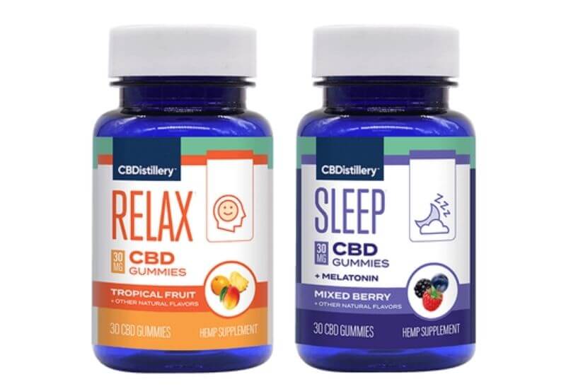 A bottle of CBDistillery tropical fruit and mixed berry CBD gummies standing side by side.