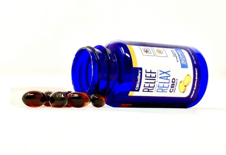Bottle of CBDistillery full spectrum softgels laying on its side with a pile of softgels spilling out.