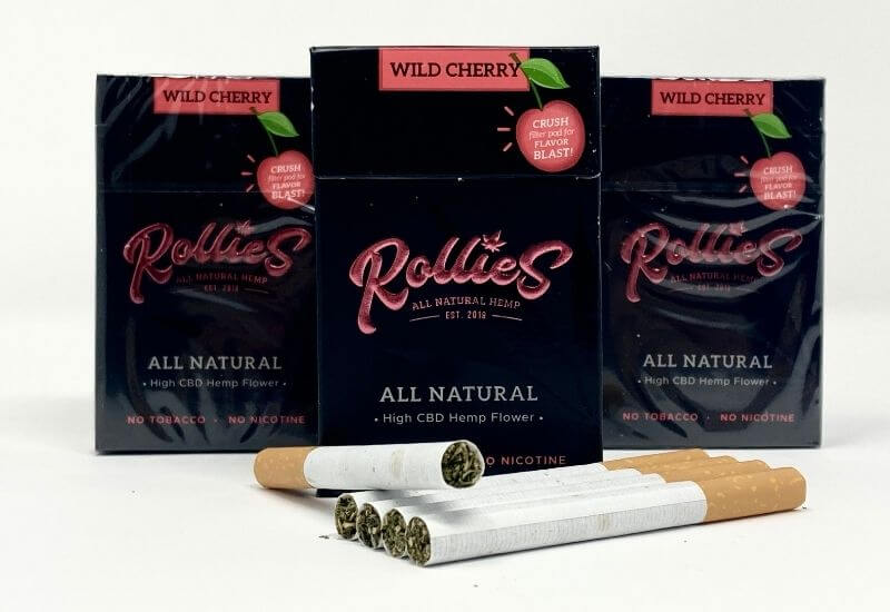 3 packs of Rollies cherry high CBD hemp flower cigarettes with 5 cigarettes laying in front.