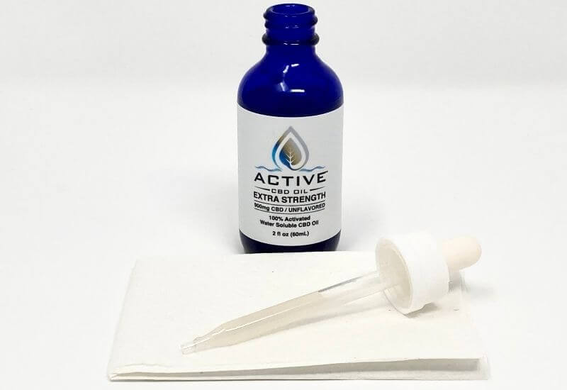 Active water soluble CBD bottle with the eyedropper full laying on a paper towel in front.