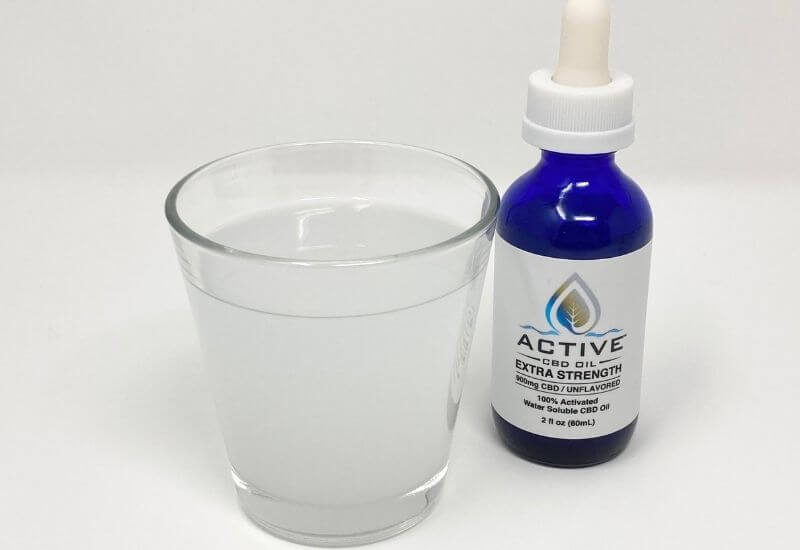 Glass of water with Active water soluble CBD mixed into it and the bottle next to the glass. The water is an opaque color.