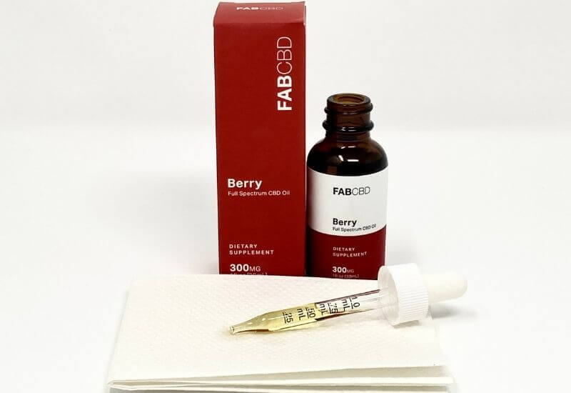 FAB CBD berry CBD oil bottle and box with an eyedropper full of oil laying on a paper towel in front.