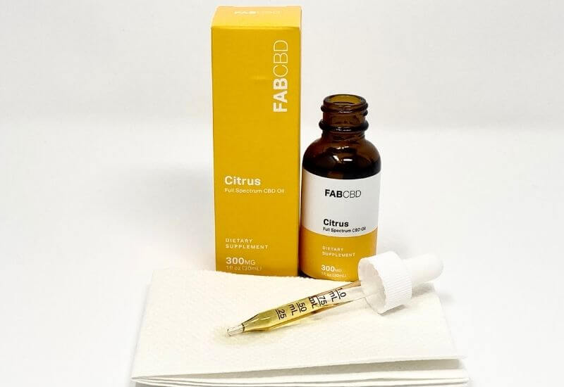 FAB CBD citrus CBD oil bottle and box with an eyedropper full of oil laying on a paper towel in front.