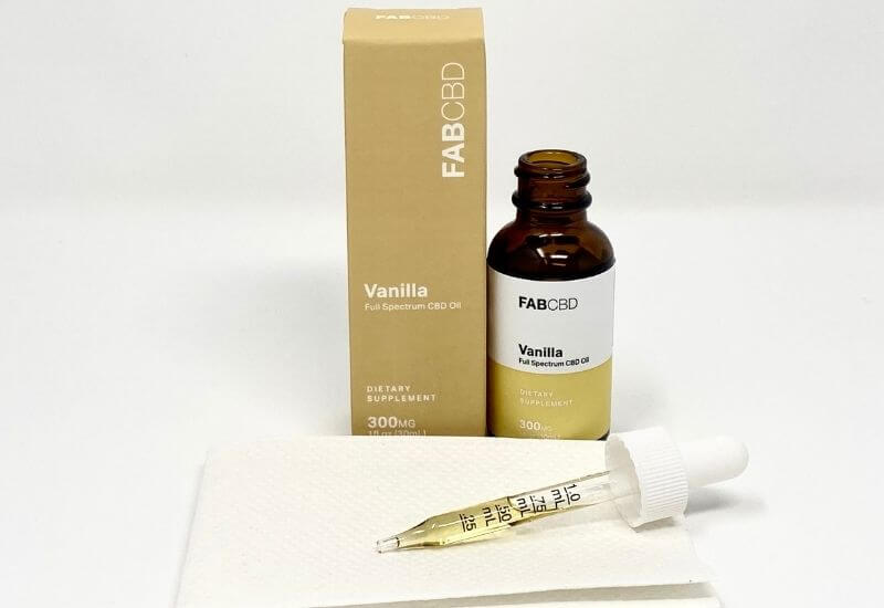 FAB CBD vanilla CBD oil bottle and box with an eyedropper full of oil laying on a paper towel in front.